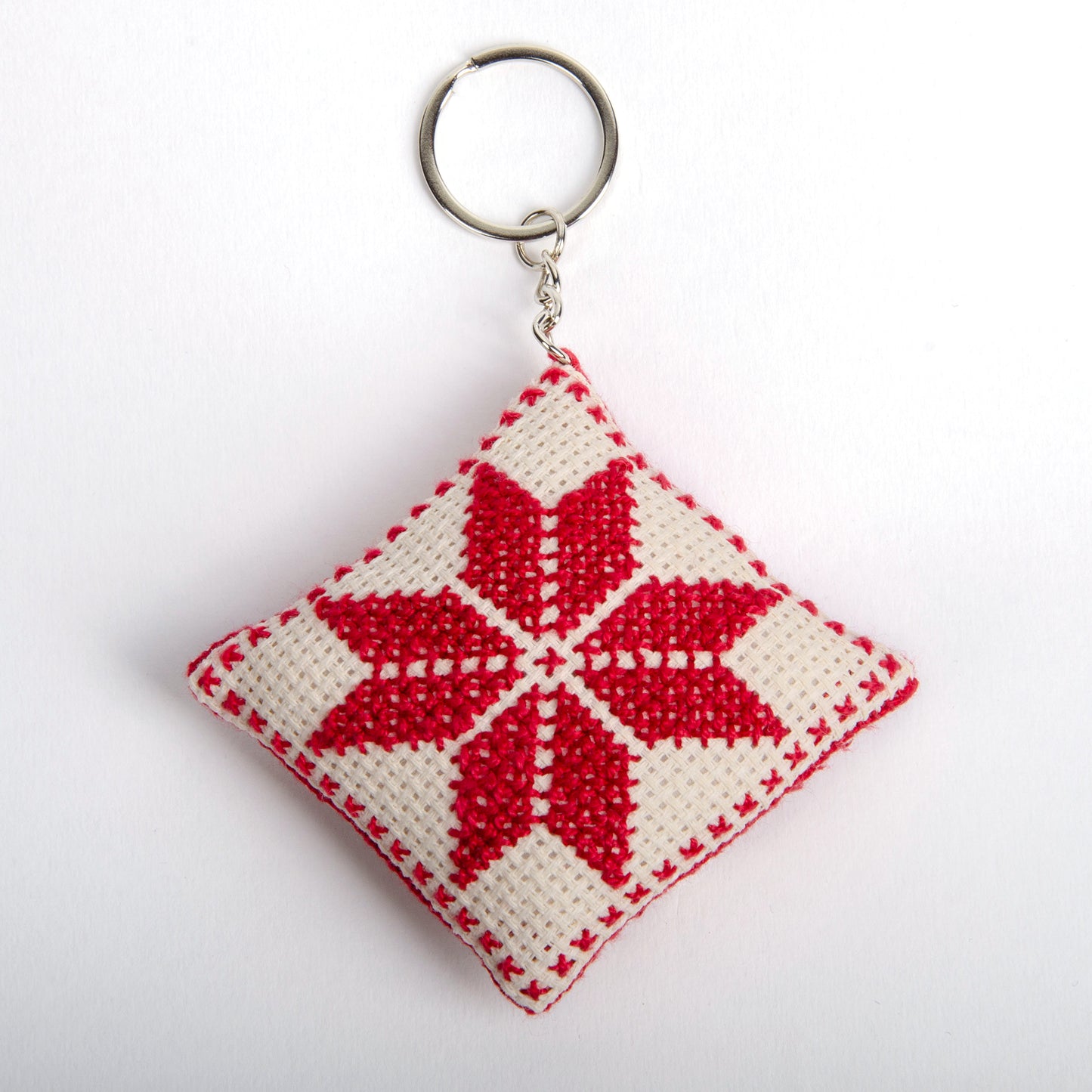 front view of a handmade Palestinian Tatreez keychain (6x6 cm) featuring traditional embroidery in white and red
colors on a small square pillow.