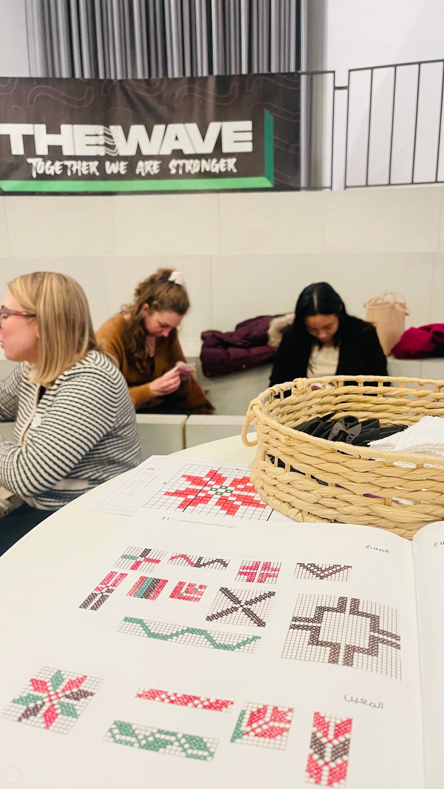 Close-up of a book displaying Palestinian Tatreez patterns, with blurred participants in a workshop setting