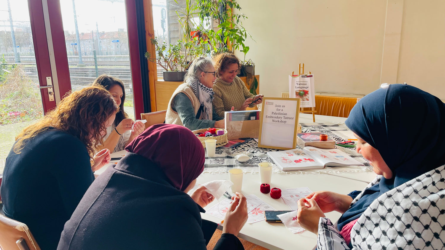 Six women gathered around a table, creating Palestinian Tatreez embroidery and sharing conversations at Oog in Oog met Palestina in Den Bosch, December 22, 2024.