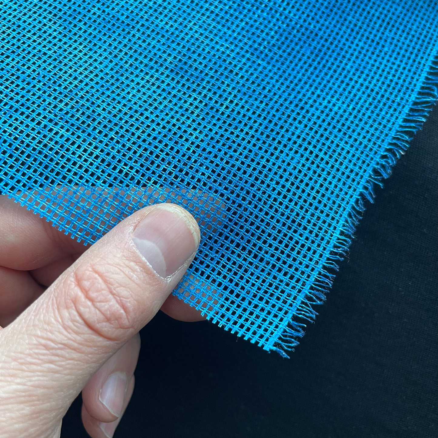 Hand holding blue 12ct waste canvas showing texture and flexibility