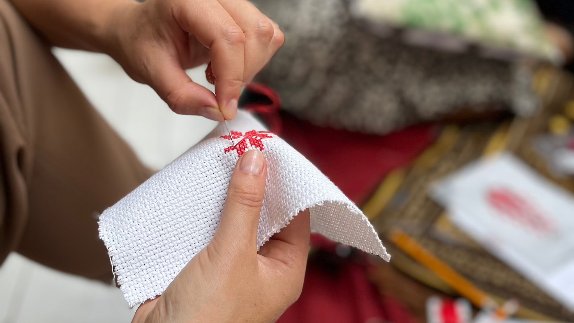 Close-up photo of a girl's hands stitching a red-colored Palestinian Tatreez pattern.