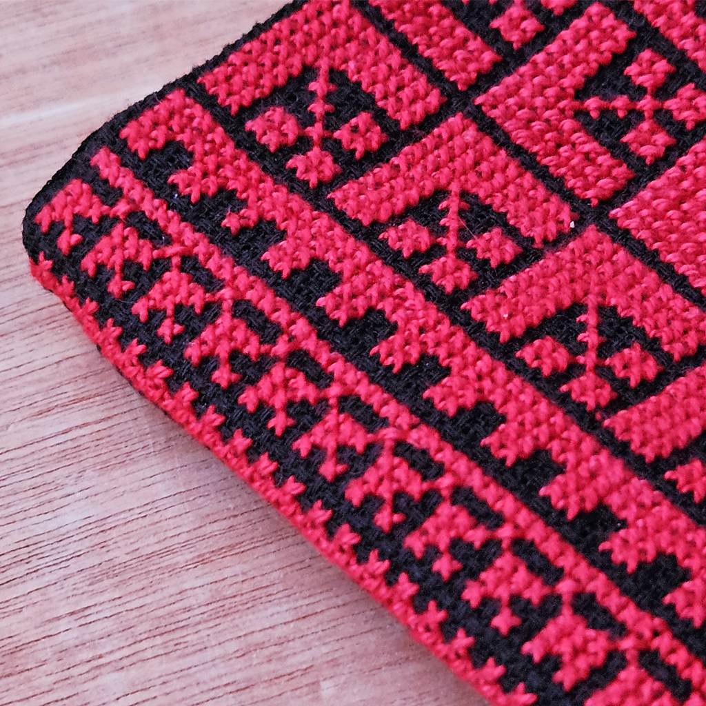 Detailed close-up of the Nafnoof eyeglasses case, showcasing its bold red and black Palestinian Tatreez embroidery and geometric border pattern.