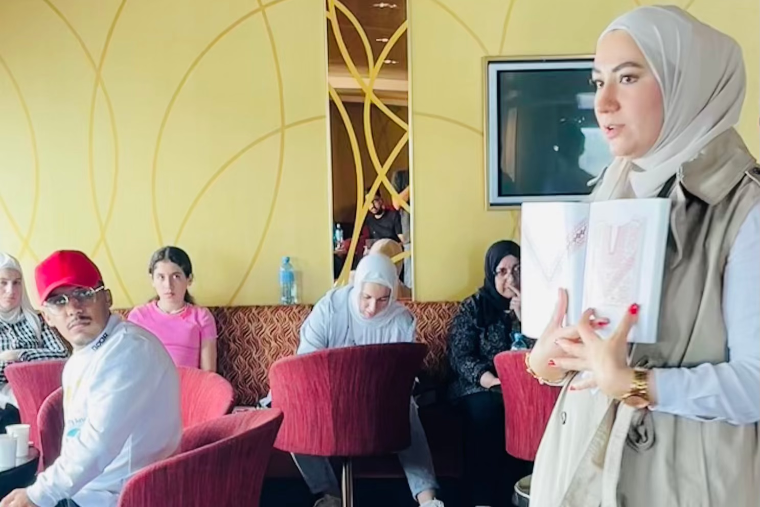 Ghenva Alkabra holding a Tatreez pattern book, passionately explaining Palestinian embroidery designs during the Galaxy Ship event.