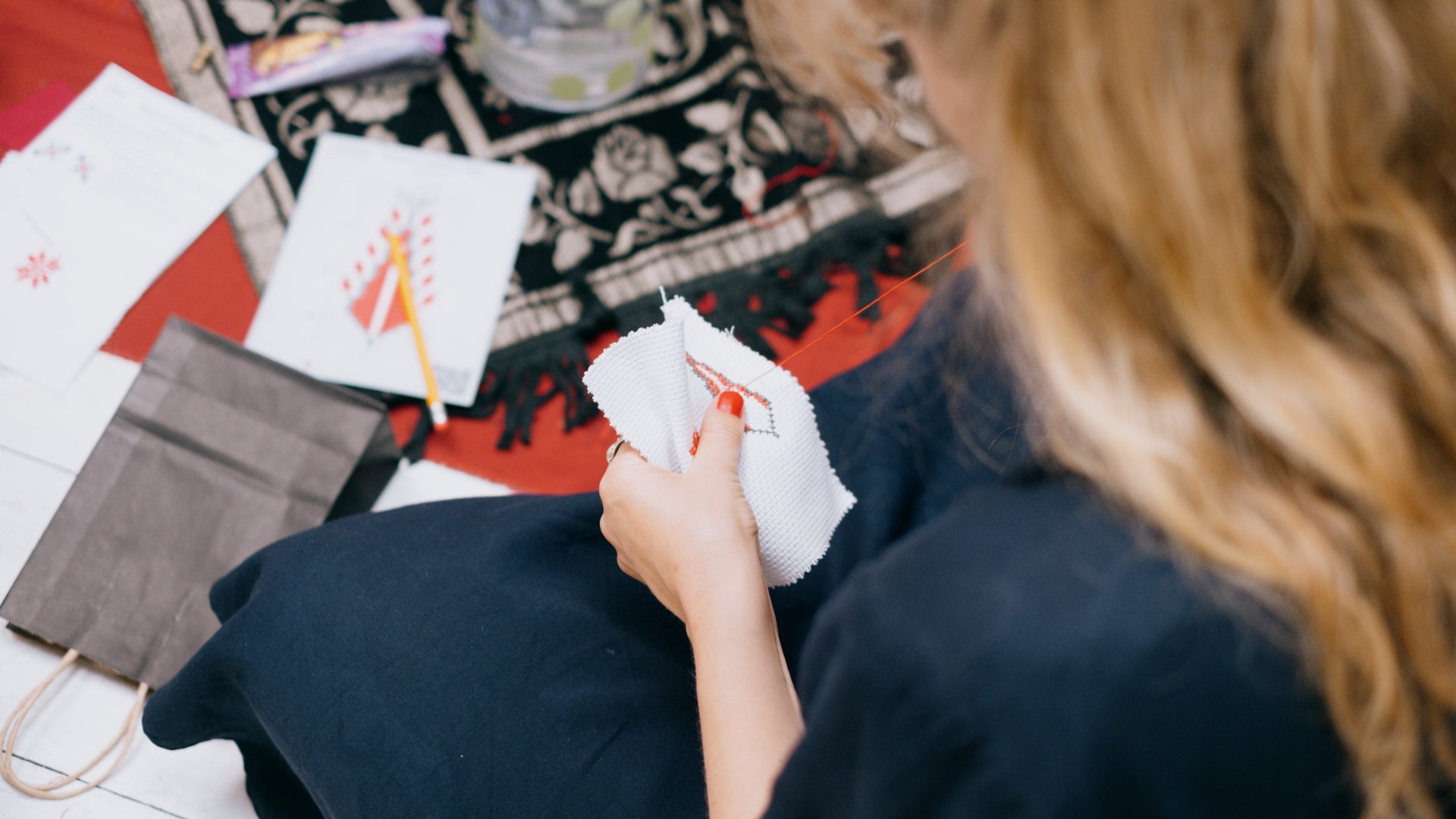 A girl from behind working on a Tatreez project, creating a detailed cypress pattern with focused hands.