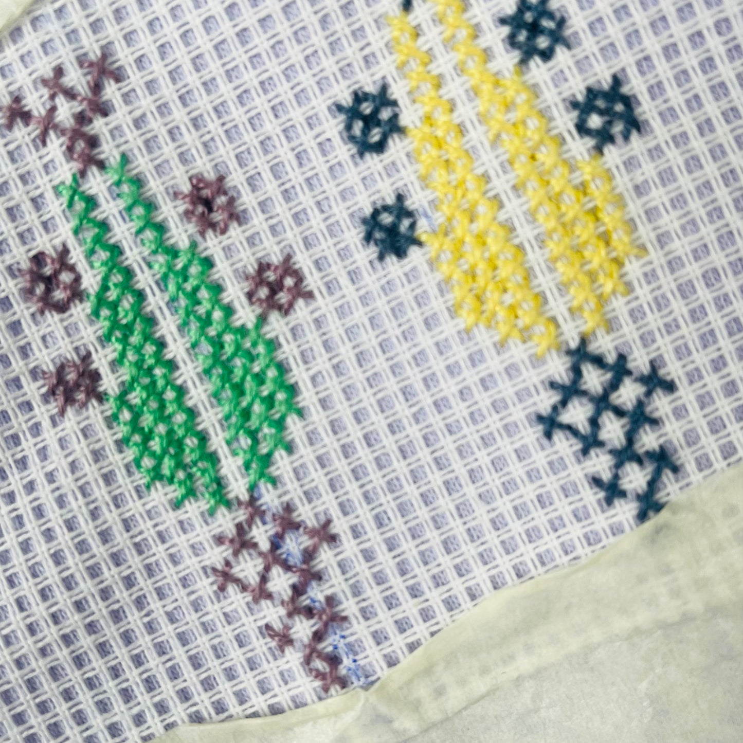 Tatreez embroidery pattern stitched on grid fabric showing colorful geometric motifs used for learning Palestinian cross-stitch.