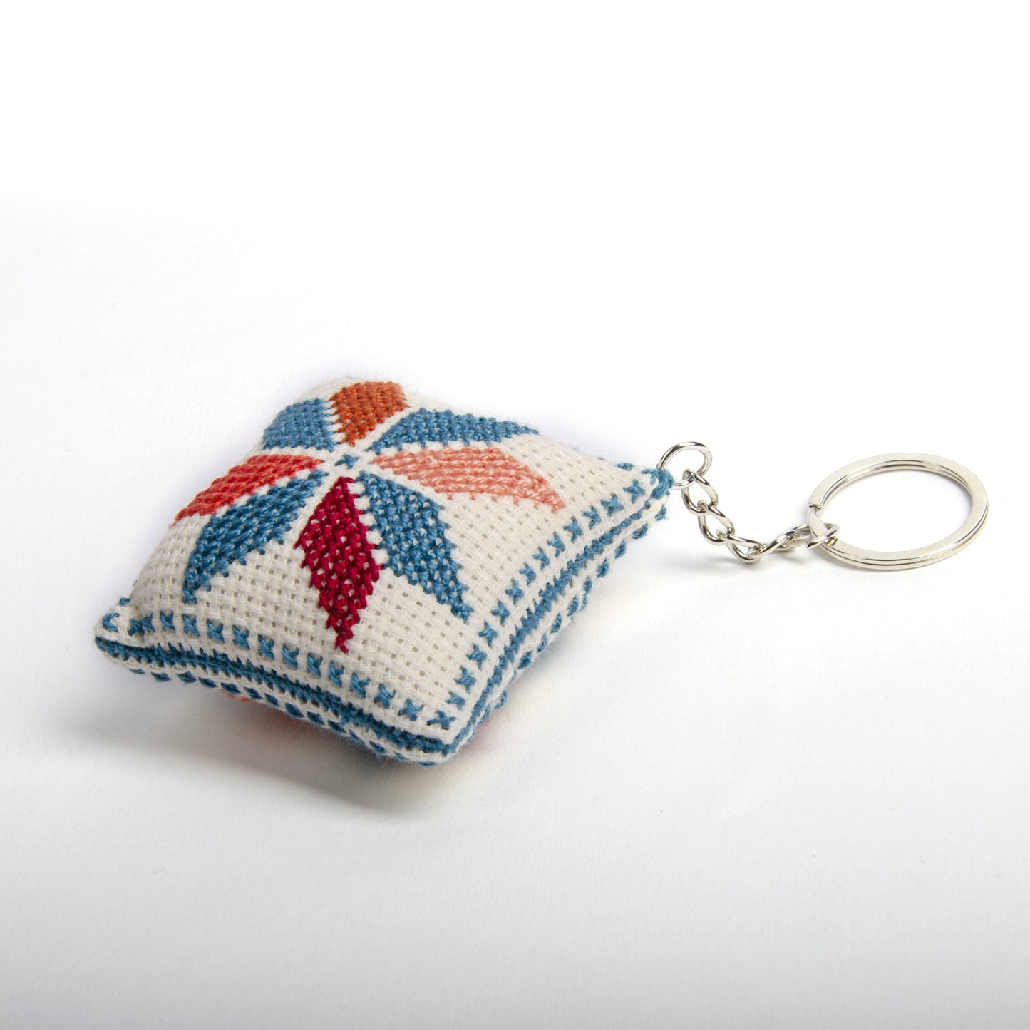 left view of a handmade Palestinian Tatreez keychain (6x6 cm) featuring traditional embroidery in blue, orange, and sky colors on a small square pillow.