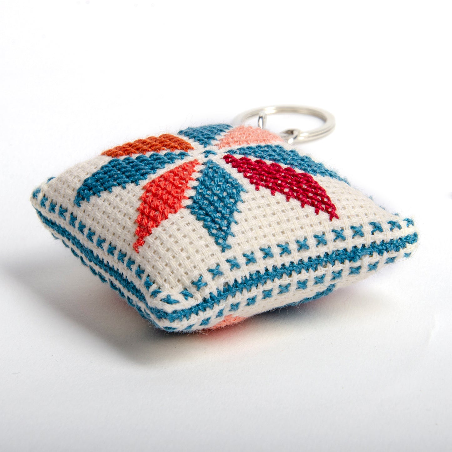 right view of a handmade Palestinian Tatreez keychain (6x6 cm) featuring traditional embroidery in blue, orange, and sky colors on a small square pillow.