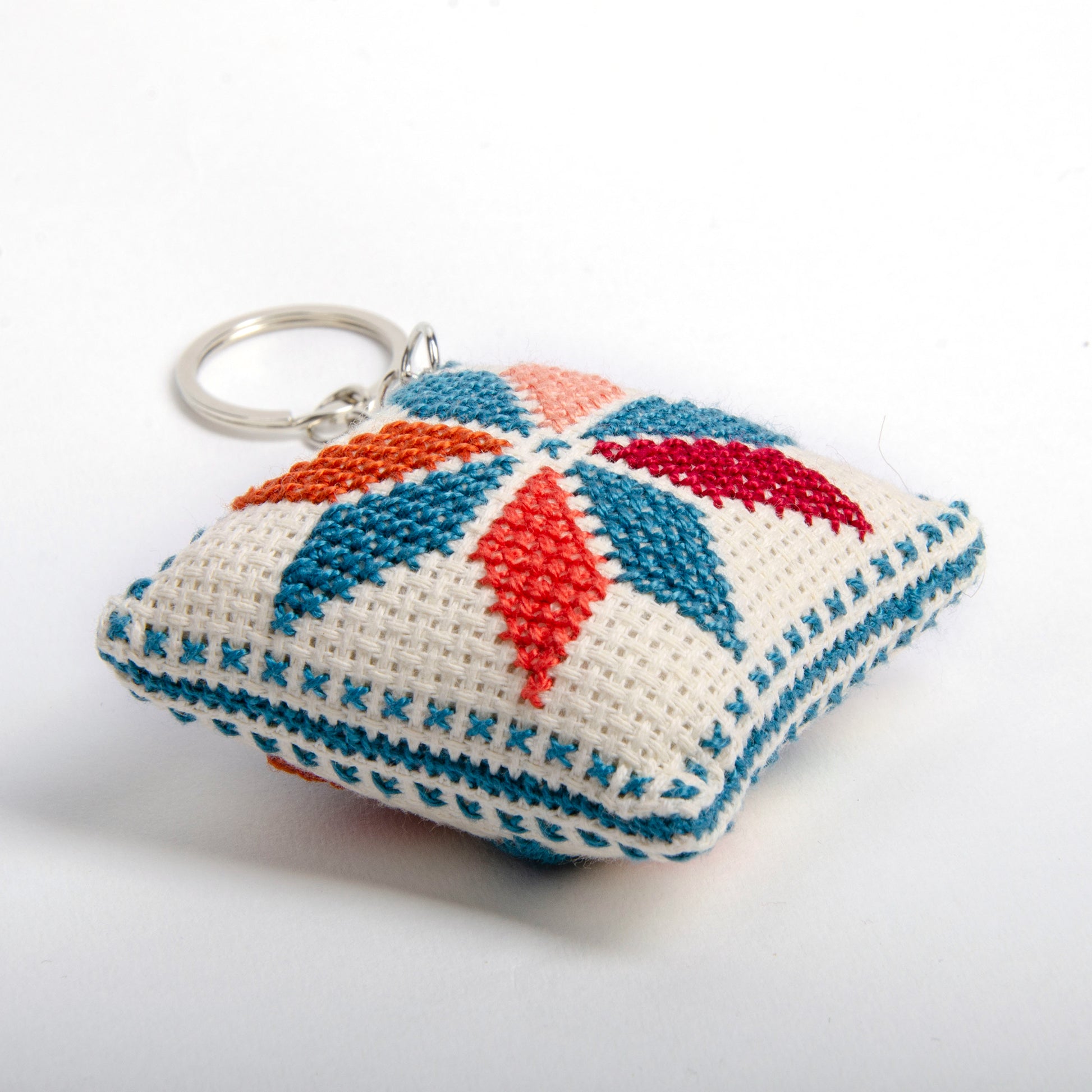 side view of a handmade Palestinian Tatreez keychain (6x6 cm) featuring traditional embroidery in blue, orange, and sky colors on a small square pillow.
