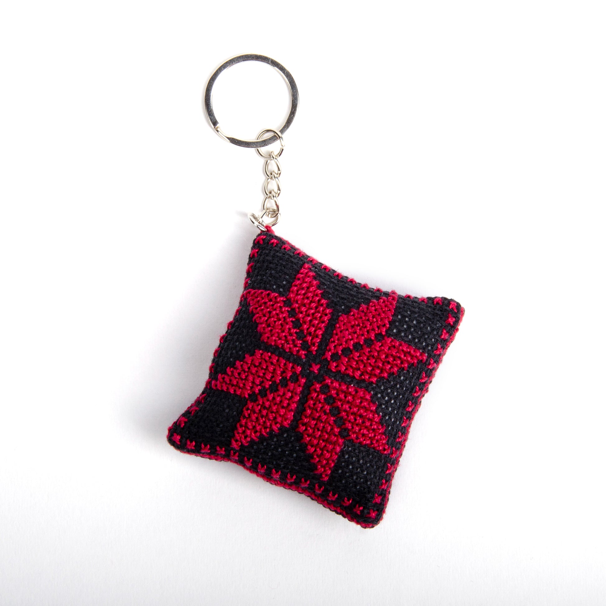 front view of a handmade Palestinian Tatreez keychain (6x6 cm) featuring traditional embroidery in balck and red
colors on a small square pillow.