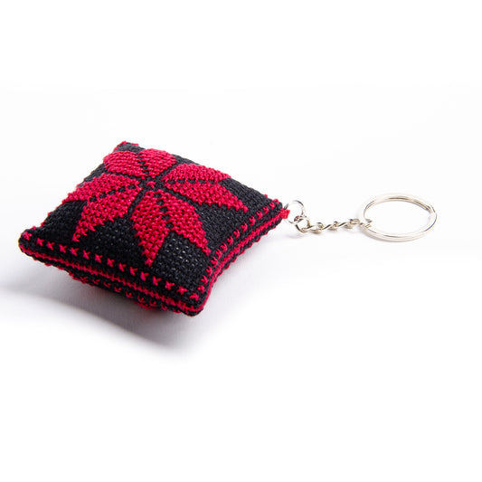 Side view of a handmade Palestinian Tatreez keychain (6x6 cm) featuring traditional embroidery in balck and red
colors on a small square pillow.