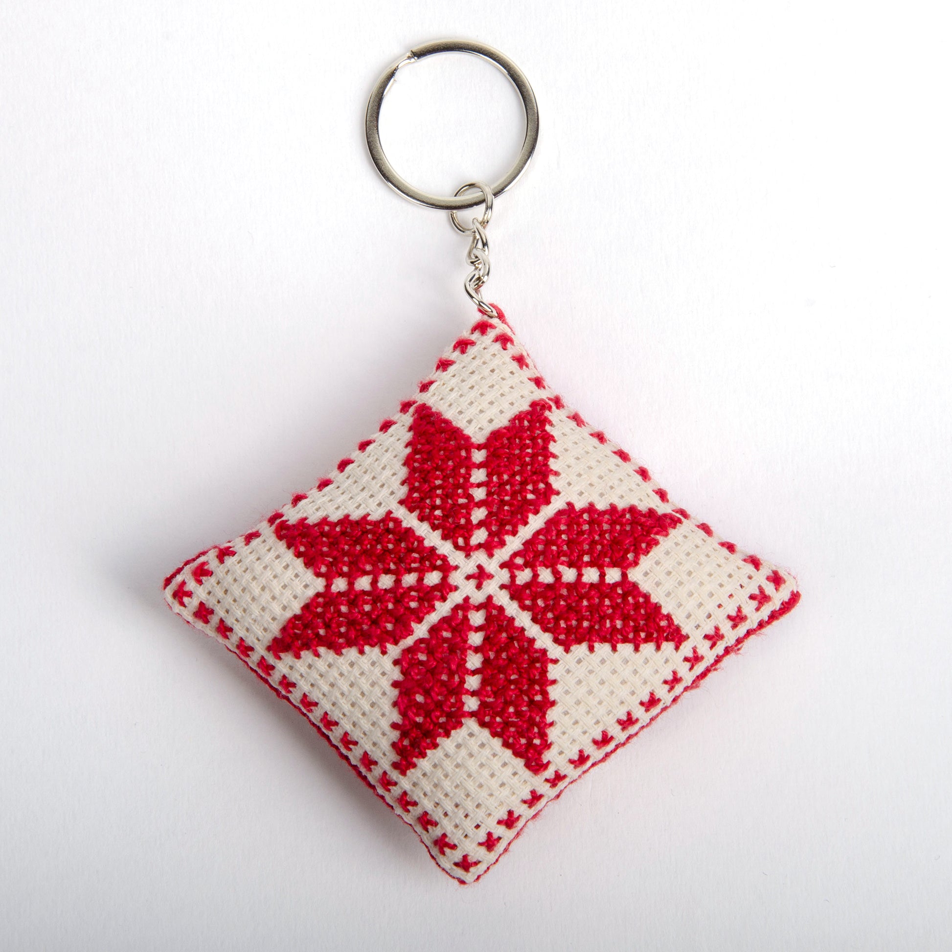 front view of a handmade Palestinian Tatreez keychain (6x6 cm) featuring traditional embroidery in white and red
colors on a small square pillow.