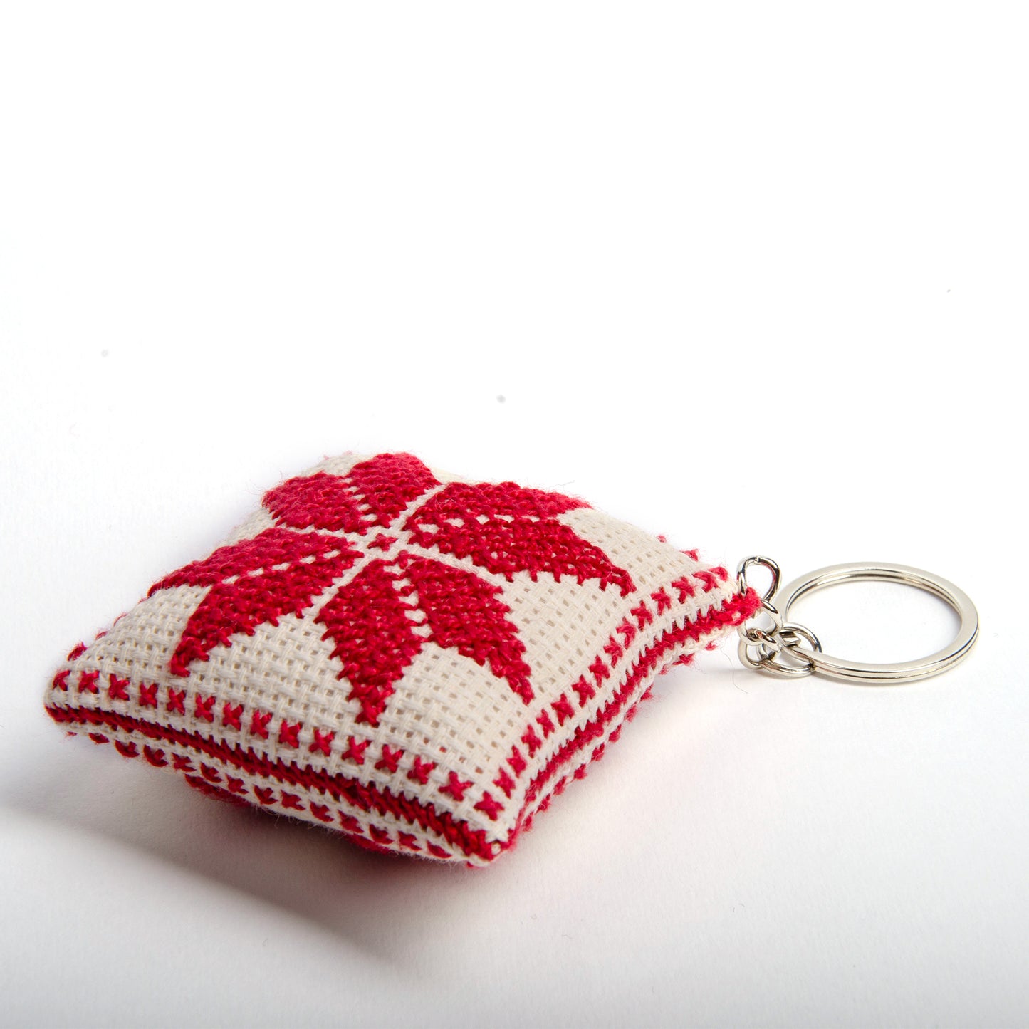 side view of a handmade Palestinian Tatreez keychain (6x6 cm) featuring traditional embroidery in white and red
colors on a small square pillow.