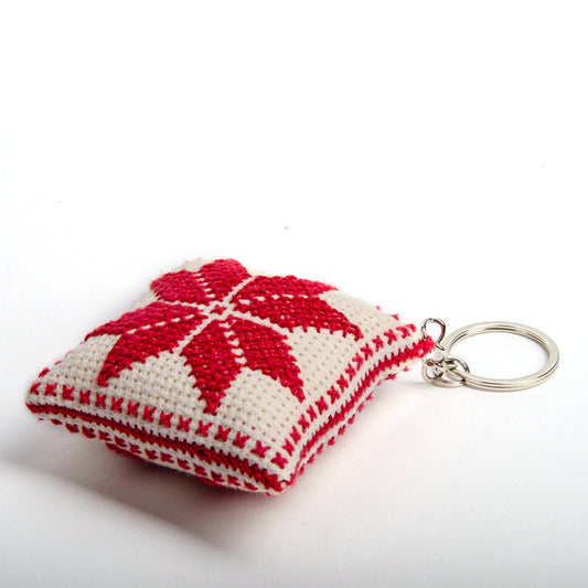 side view of a handmade Palestinian Tatreez keychain (6x6 cm) featuring traditional embroidery in white and red
colors on a small square pillow.