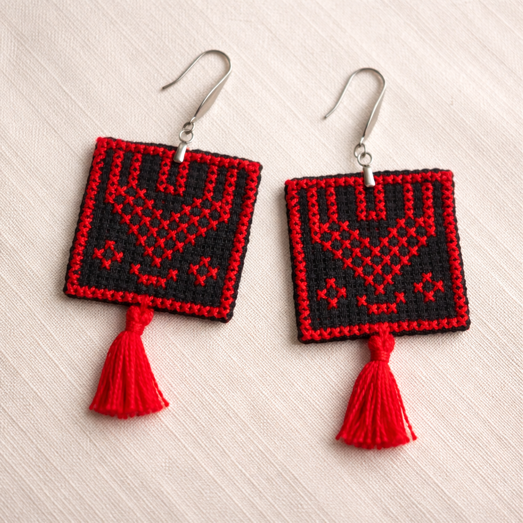 Ramallah thobe panel inspired Palestinian Tatreez embroidered earrings on textile background with red tassel