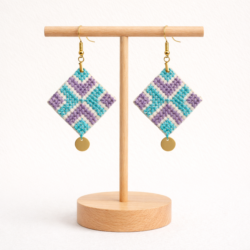 Front view of Reesh Palestinian Tatreez embroidered earrings on wooden stand