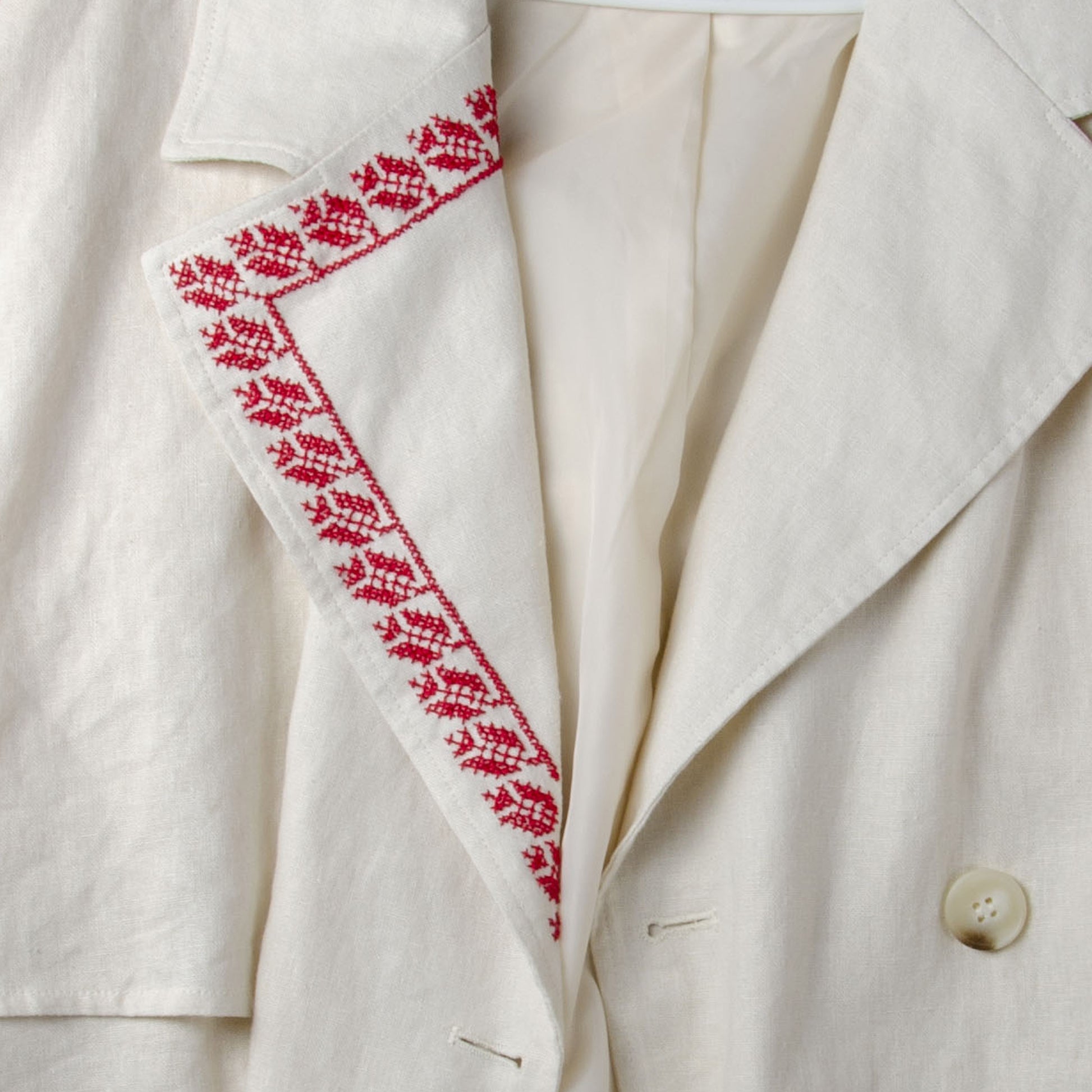 Traditional Palestinian tatreez embroidery stitched along the sleeve of a light-colored jacket using red cross-stitch patterns.