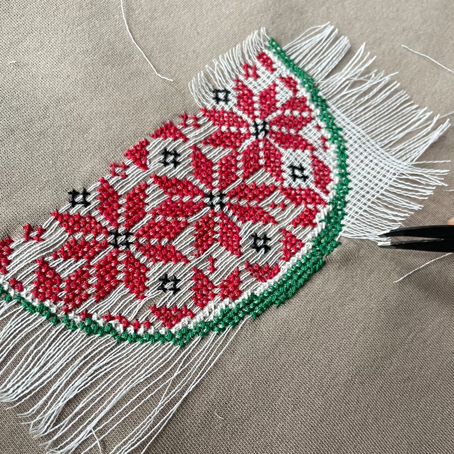 Close-up of Palestinian tatreez cross-stitch embroidery on clothing featuring a traditional red geometric motif stitched on fabric.