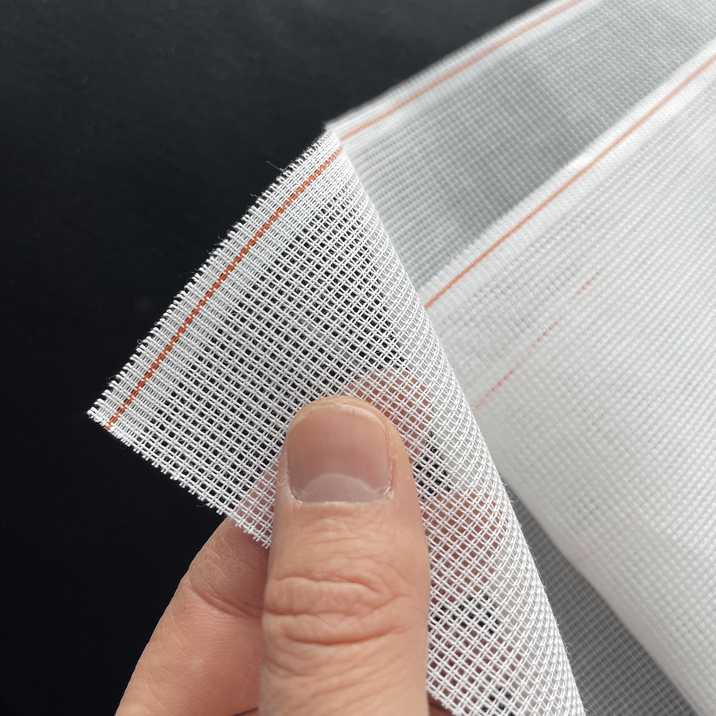 Hand holding layers of white 14ct waste canvas showing texture and flexibility