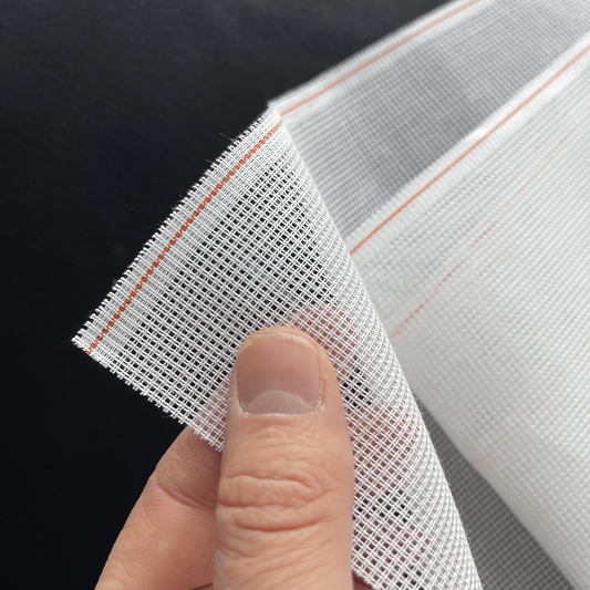 Hand holding layers of white 14ct waste canvas showing texture and flexibility