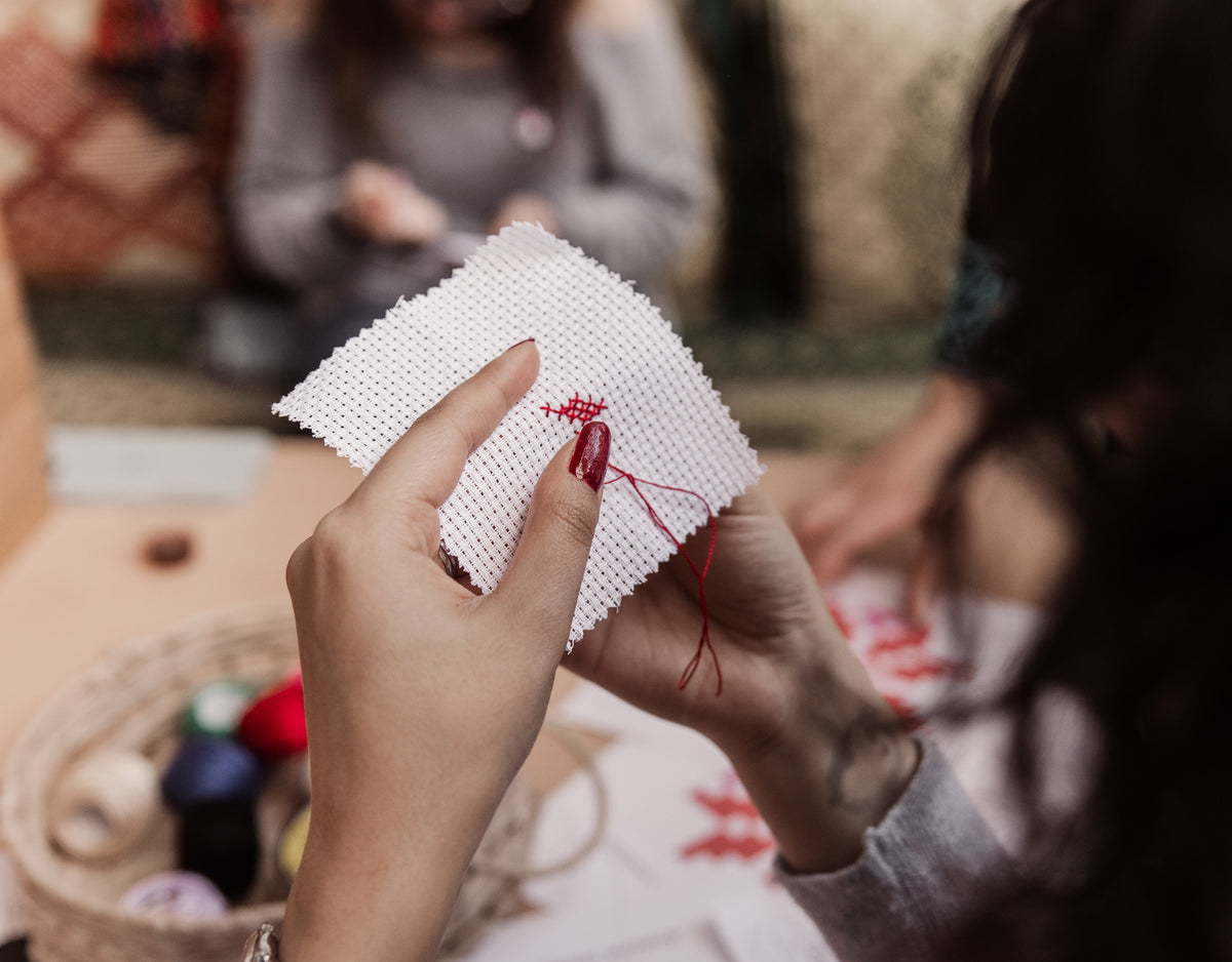 A young girl carefully stitches a traditional Palestinian Tatreez star pattern onto a small Aida cloth, holding a threaded needle during a Tatreez Language workshop.