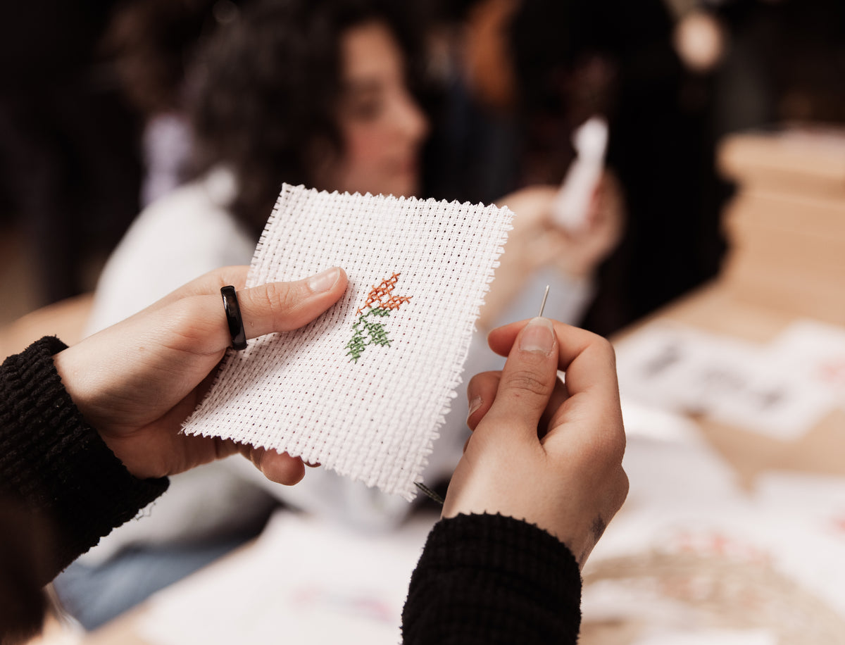 Close-up of hands holding a piece of Aida fabric with a colorful floral Palestinian Tatreez motif during a hands-on embroidery workshop.